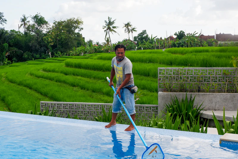 Pool technician skimming debris and testing water chemistry during a weekly visit