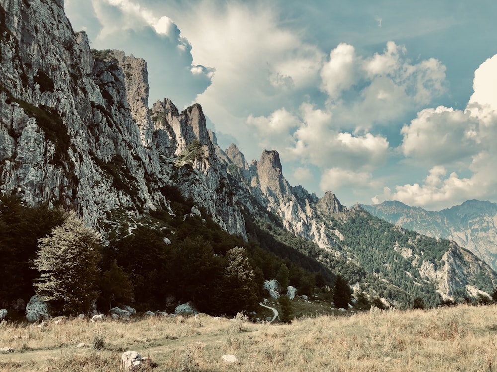 green grass field near rocky mountain under white clouds during daytime