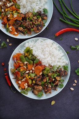 A colorful plate featuring grilled chicken, fresh vegetables, and a side of fried rice.