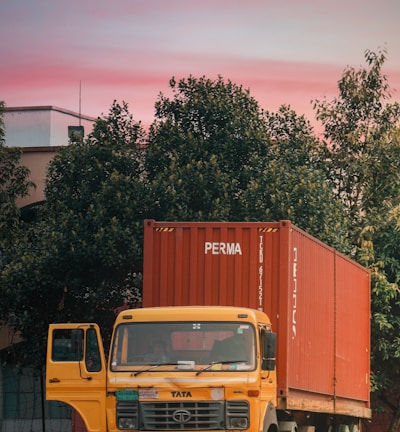 yellow truck parked beside green tree during daytime