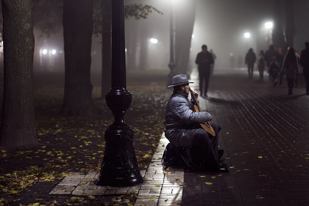 man in black jacket sitting on sidewalk during night time