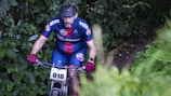 A cyclist wearing fitage b.v. gear racing through a forest trail.