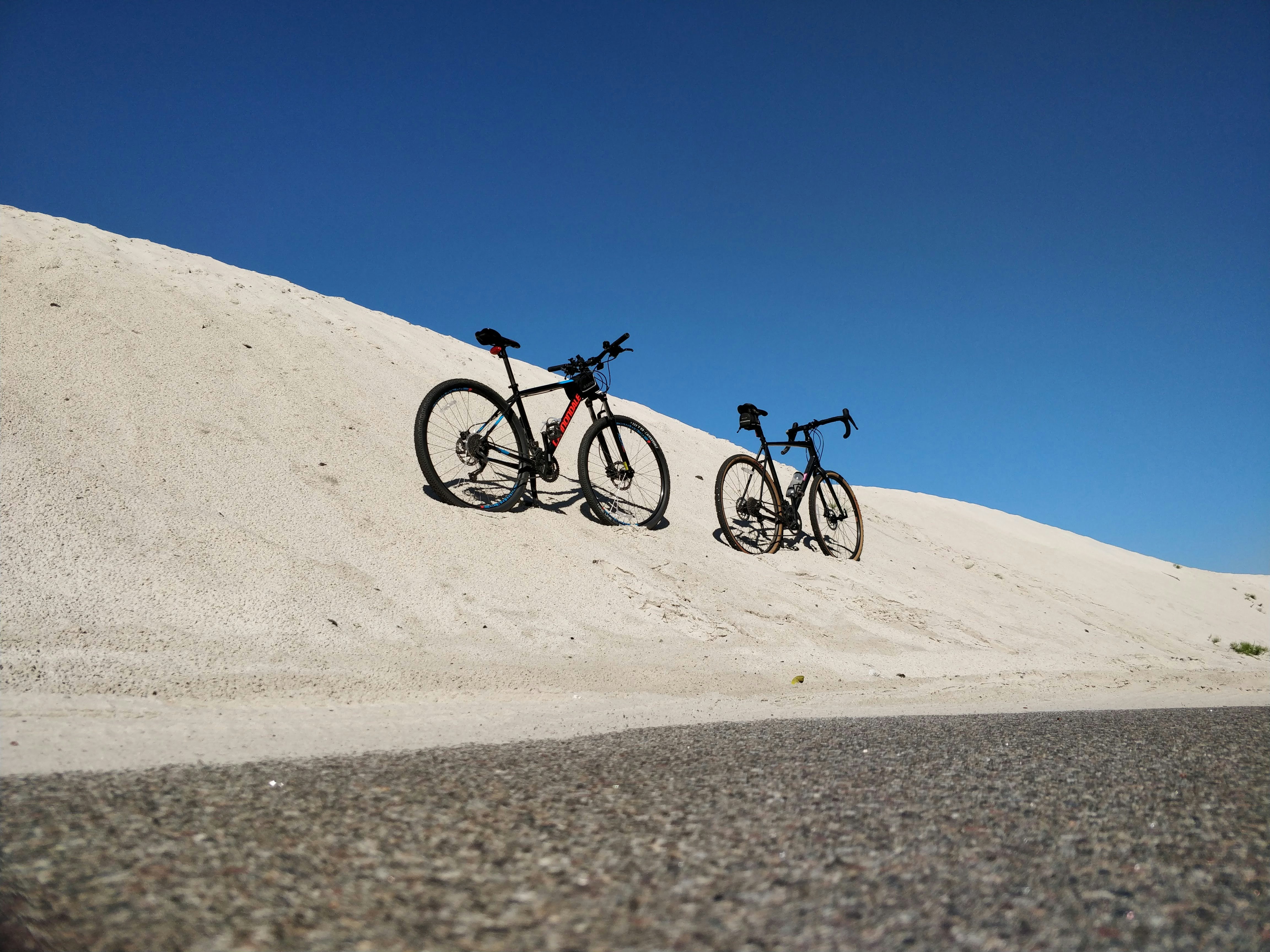 2 men riding on bicycles on white sand during daytime