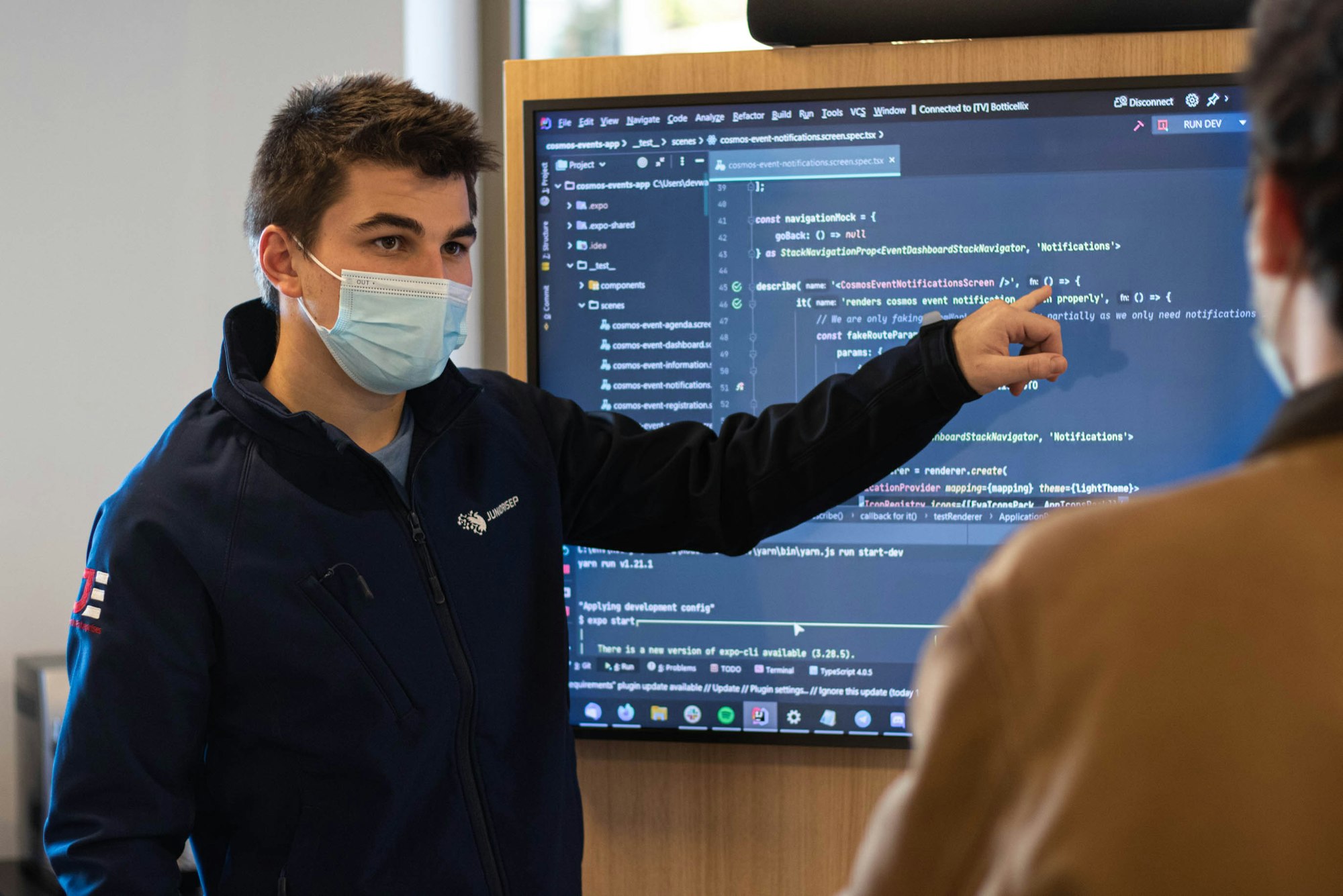 Two people working, and discussing about a presentation with code on a screen.
Student showing code on a tv.