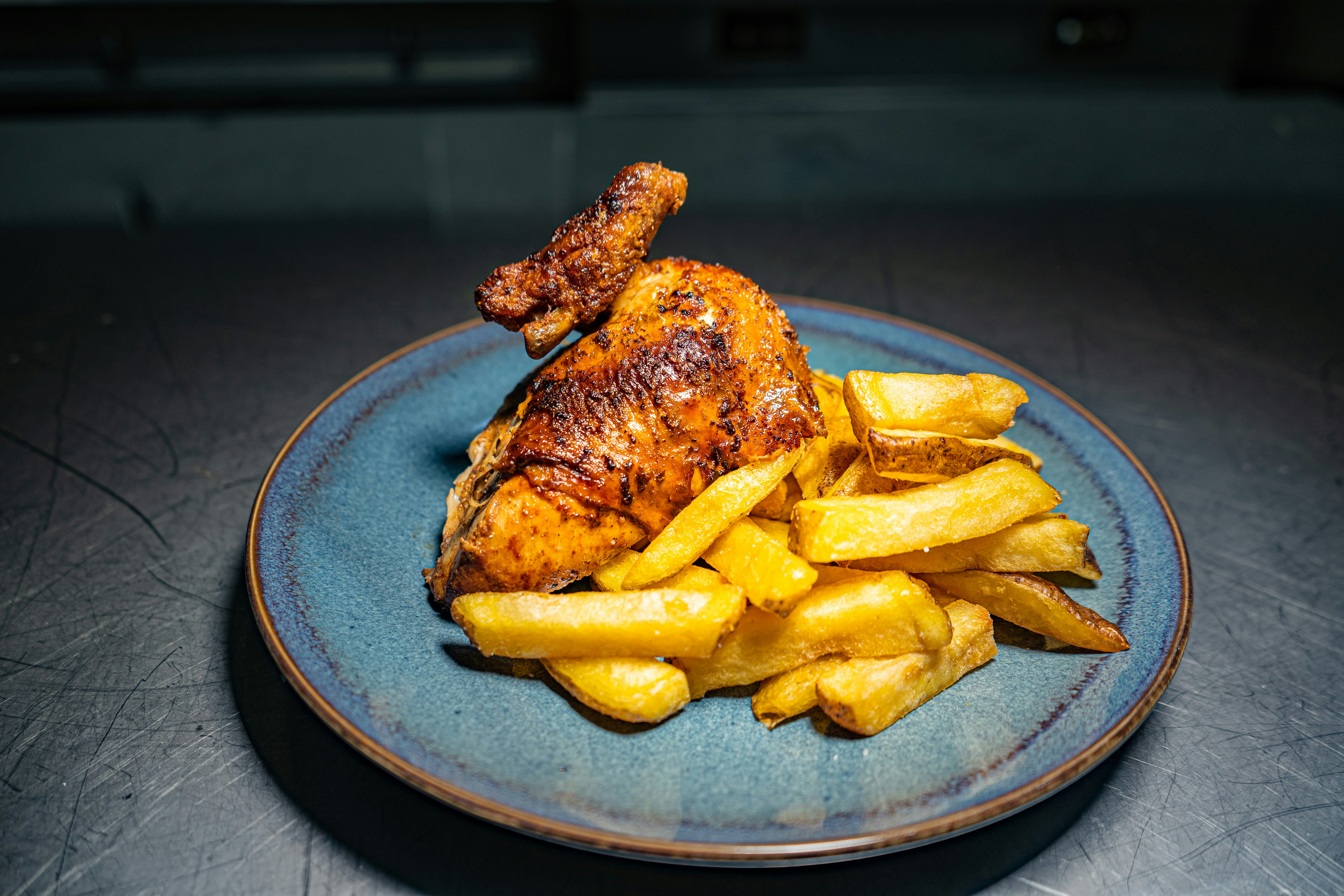 Half grilled chicken with golden char marks, rice and fries on dark plate, warm amber lighting