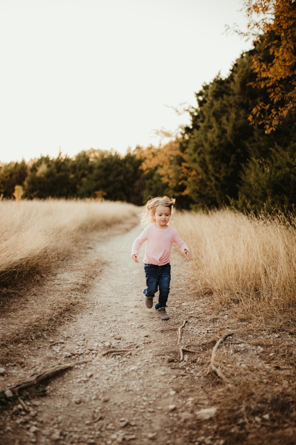 girl in white long sleeve shirt and blue denim jeans running on dirt road during daytime