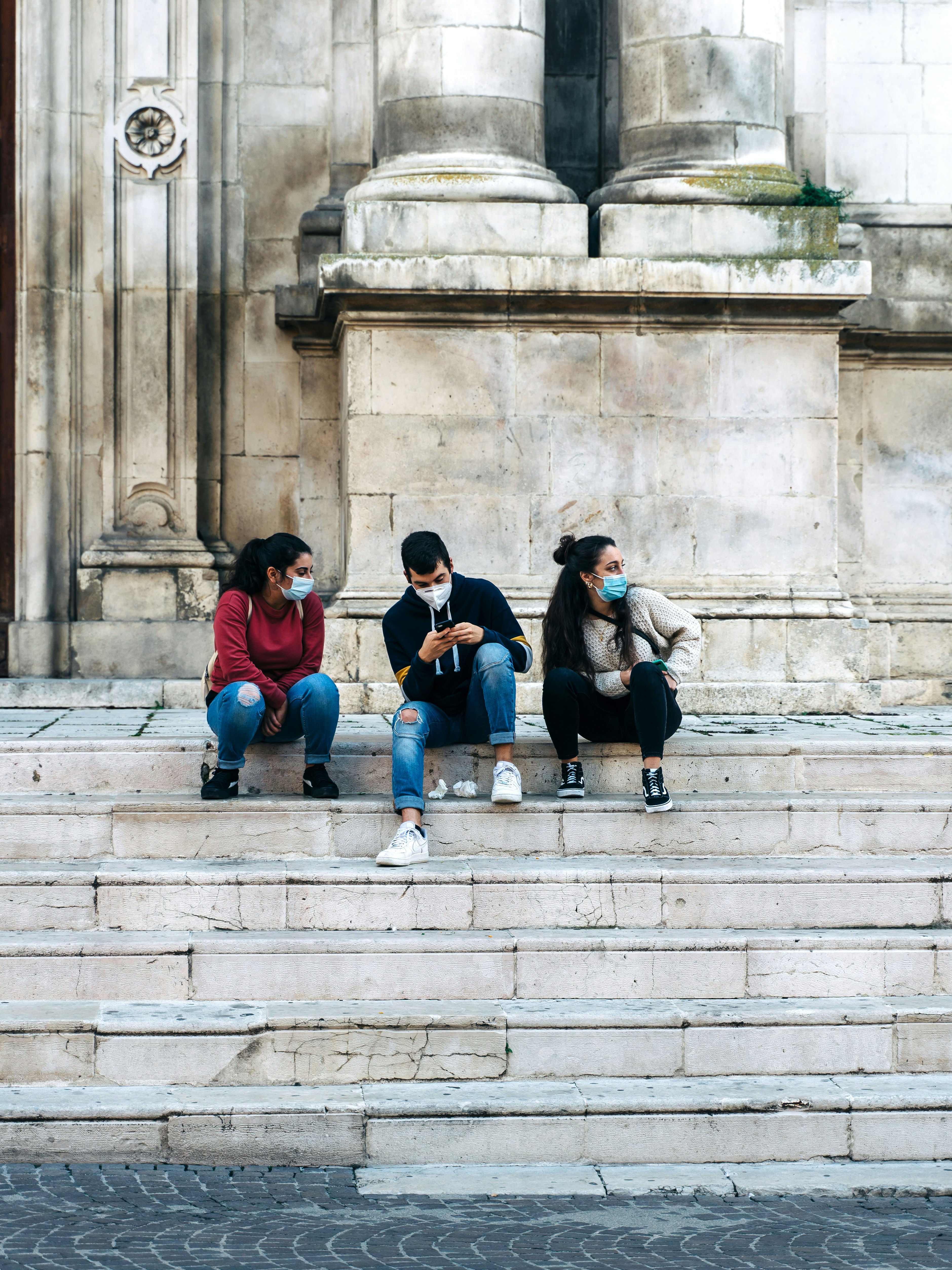 Three Italian teens chat on the marble steps of a church in Abruzzo, Italy
