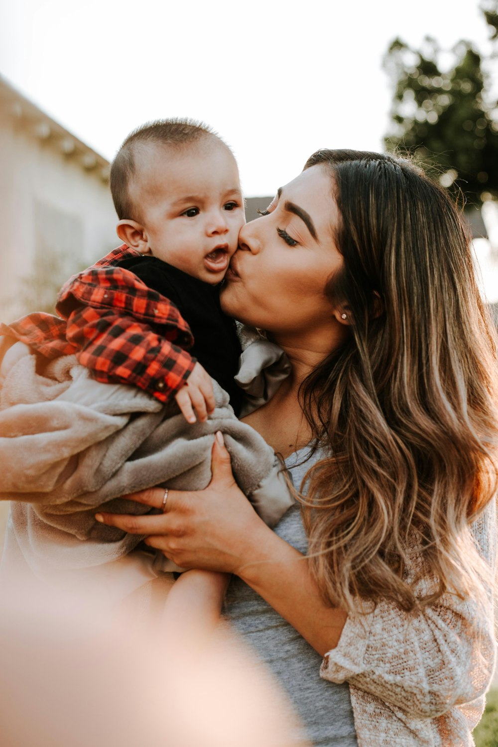 woman in white shirt carrying baby in red and black plaid shirt