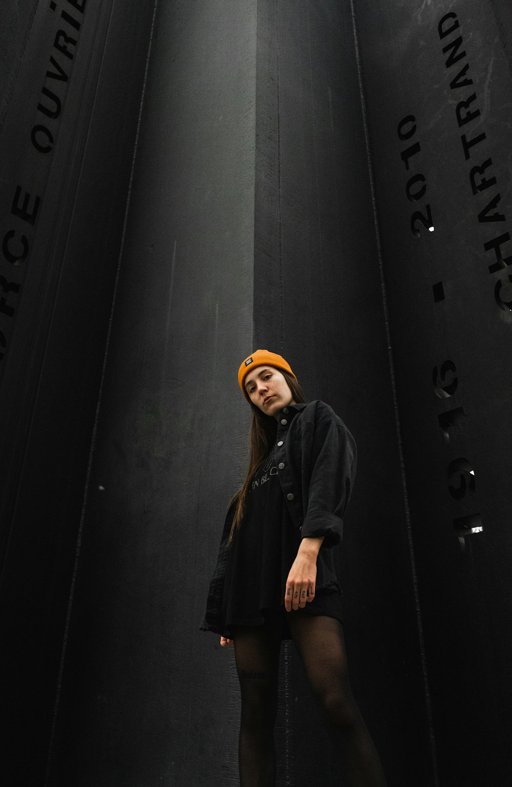 woman in black jacket standing beside black wall