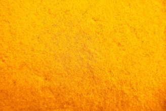 A textured surface with a rich yellow hue, exhibiting a uniform pattern resembling a close-up of a sponge or fabric.