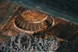 Intricate wooden carvings with a focus on a serene Buddha statue embedded in a detailed, ornate ceiling. Rich textures and patterns are highlighted, showcasing a fusion of cultural artistry and spirituality.