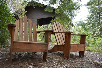 Rustic outdoor wooden chairs arranged on a leafy forest floor, inviting relaxation.