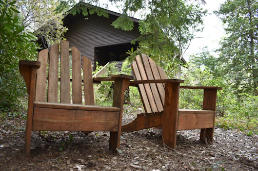 Rustic outdoor wooden chairs arranged on a leafy forest floor, inviting relaxation.