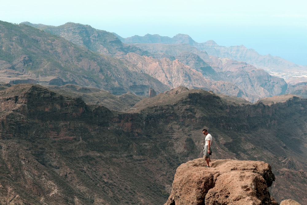 man in white shirt standing on brown rock mountain during daytime