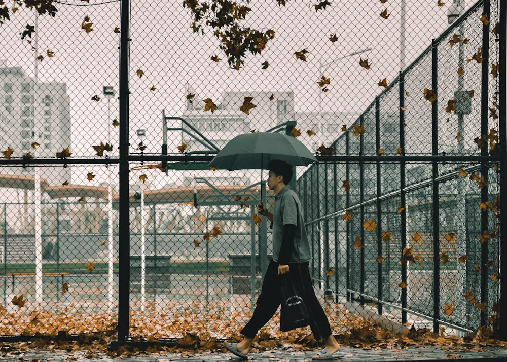 woman in gray jacket and black pants holding umbrella standing beside gray metal fence during daytime