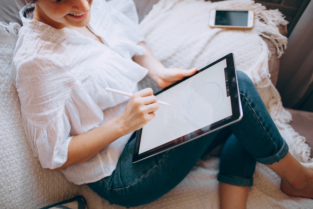 woman in white shirt and blue denim jeans holding white tablet computer