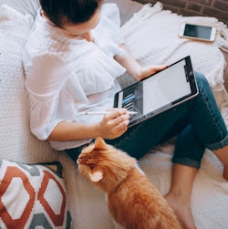 woman in white long sleeve shirt and blue denim shorts sitting on bed using tablet computer