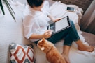 woman in white long sleeve shirt and blue denim shorts sitting on bed using tablet computer