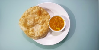 A white plate holds several puffed, golden-brown puris next to a small bowl of bright yellow curry with visible potato pieces.