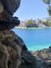 A scenic seaside spot with pastel-colored buildings and olive trees under a soft blue sky.