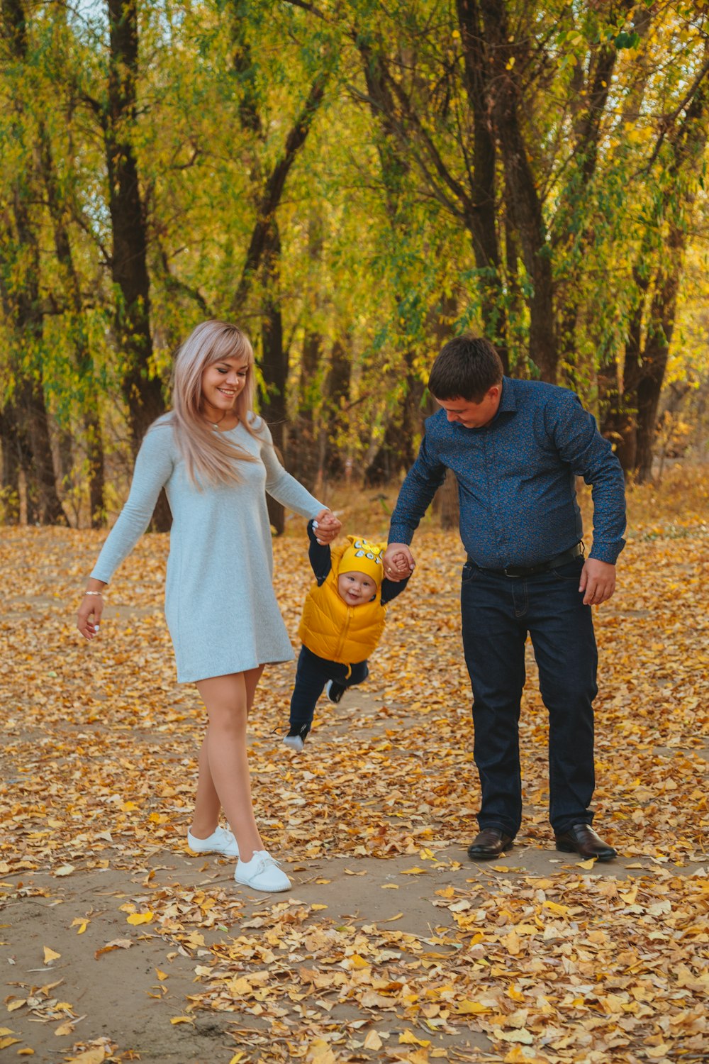 man and woman holding hands while walking on dried leaves on forest during daytime