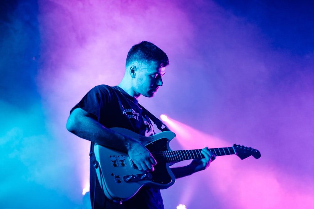 Hombre con camiseta negra de cuello redondo tocando la guitarra eléctrica