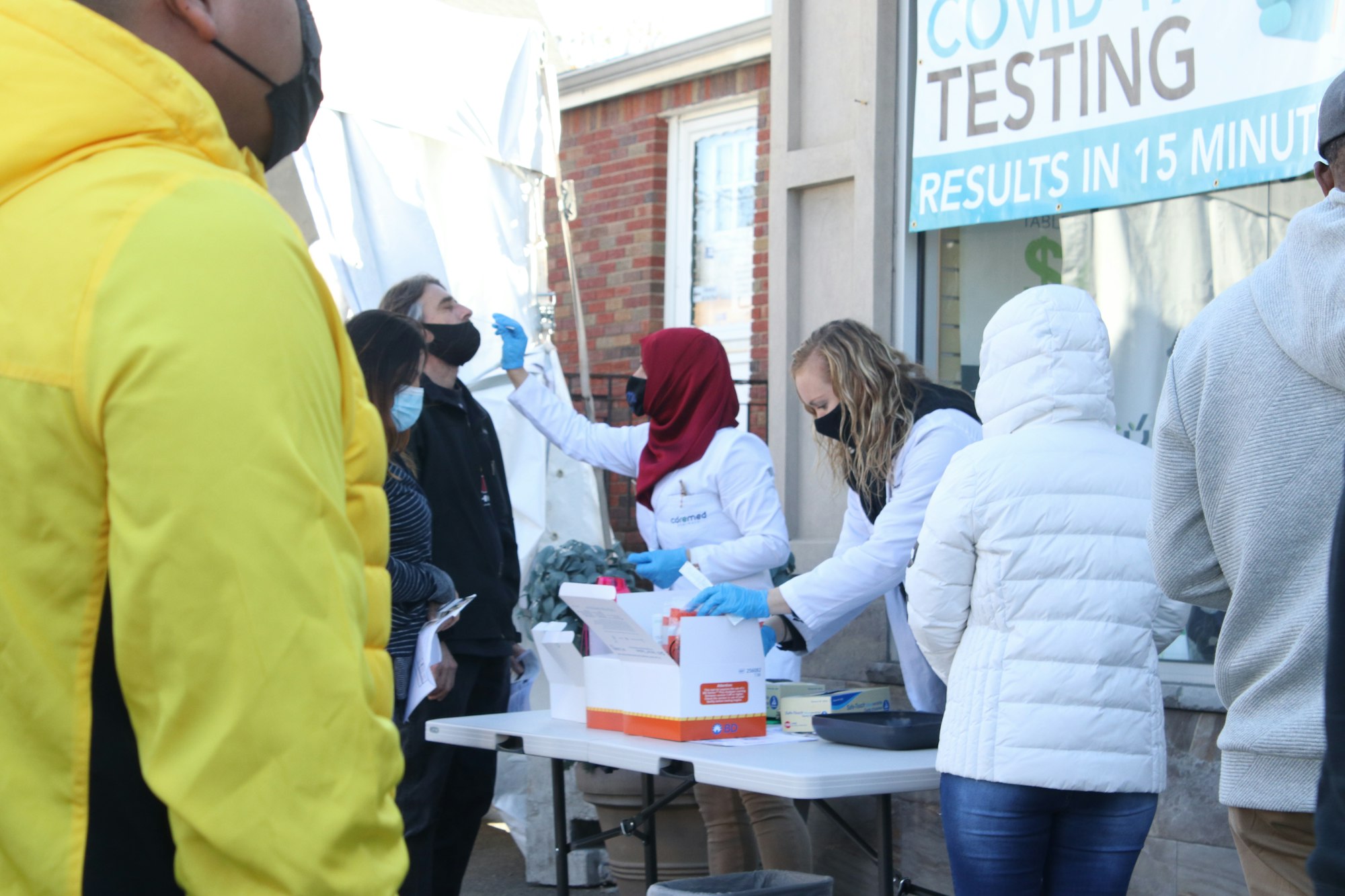 Masked medical workers conduct COVID testing outside a testing center.