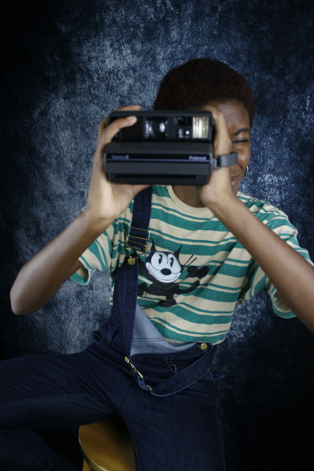boy in green and black stripe shirt holding black camera