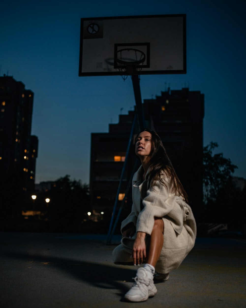 woman in white coat sitting on sidewalk during night time