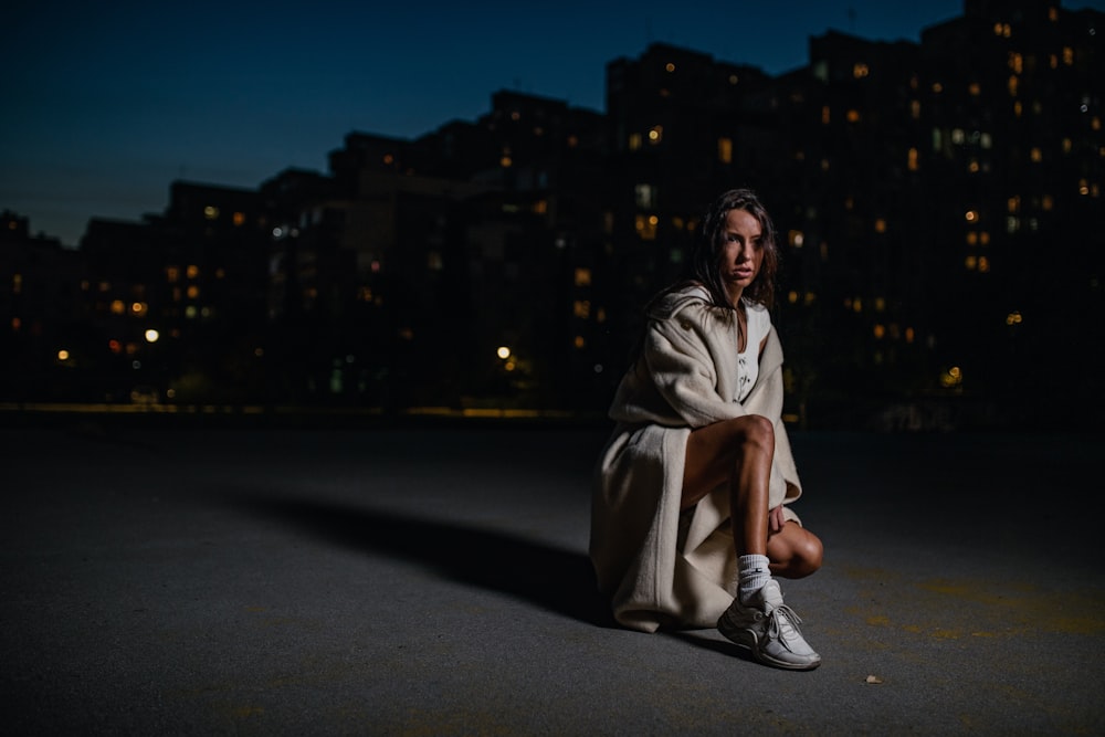 woman in brown coat sitting on the road during night time