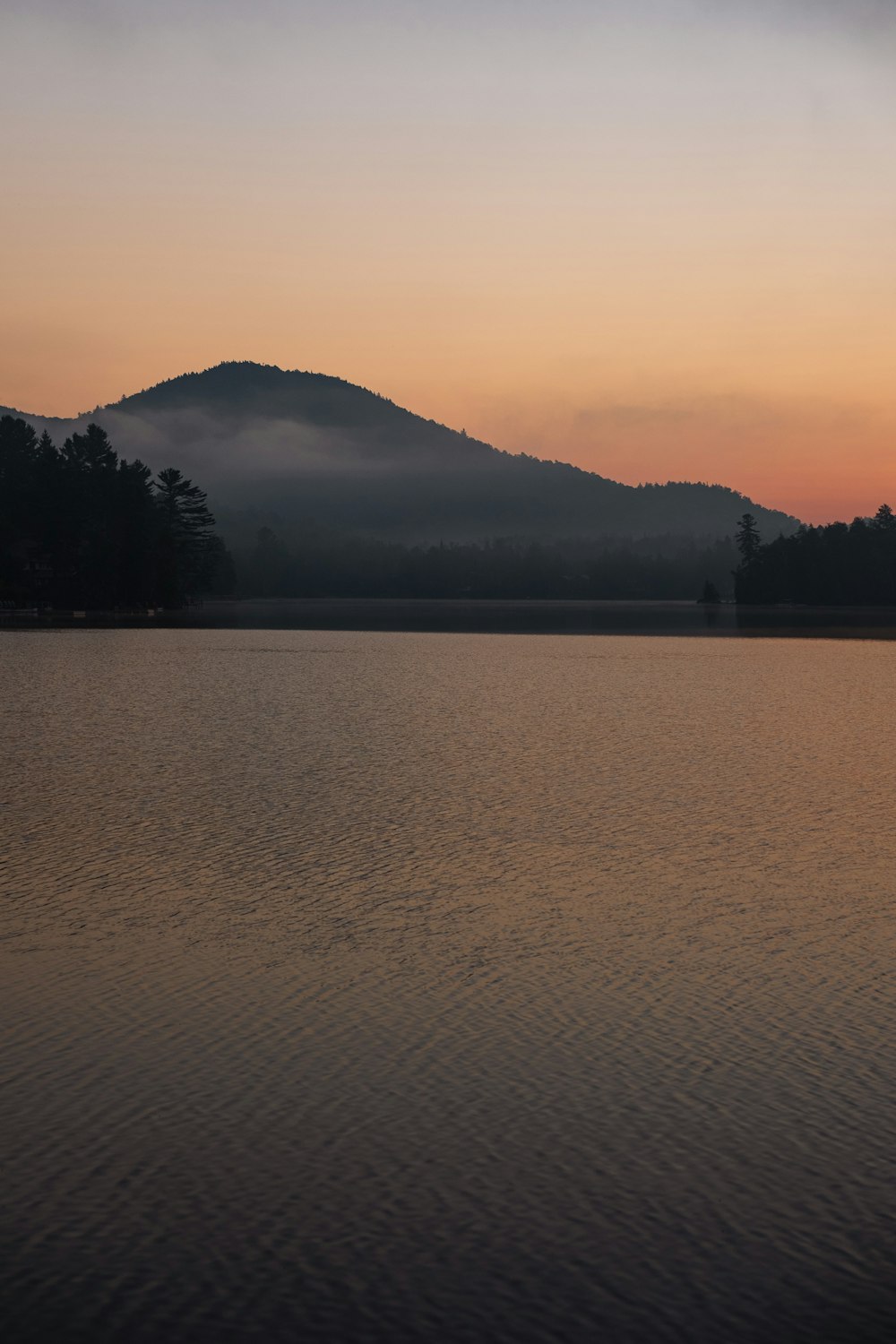 silhouette of mountain near body of water during sunset