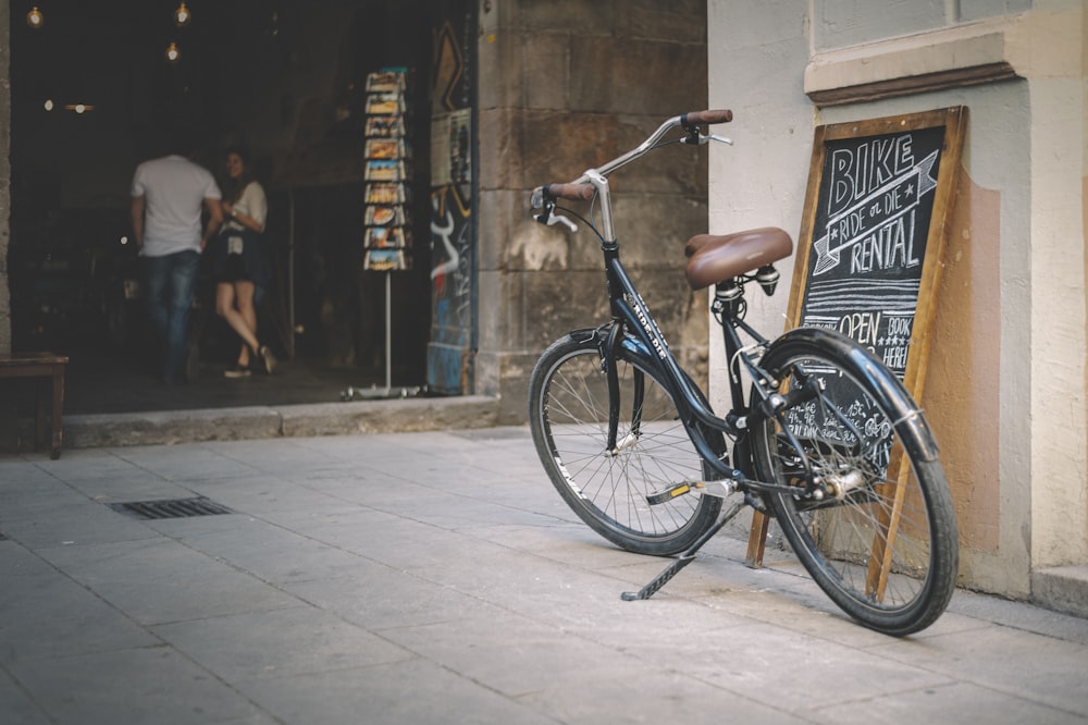 Bicicleta urbana negra estacionada al lado de un edificio de hormigón marrón durante el día