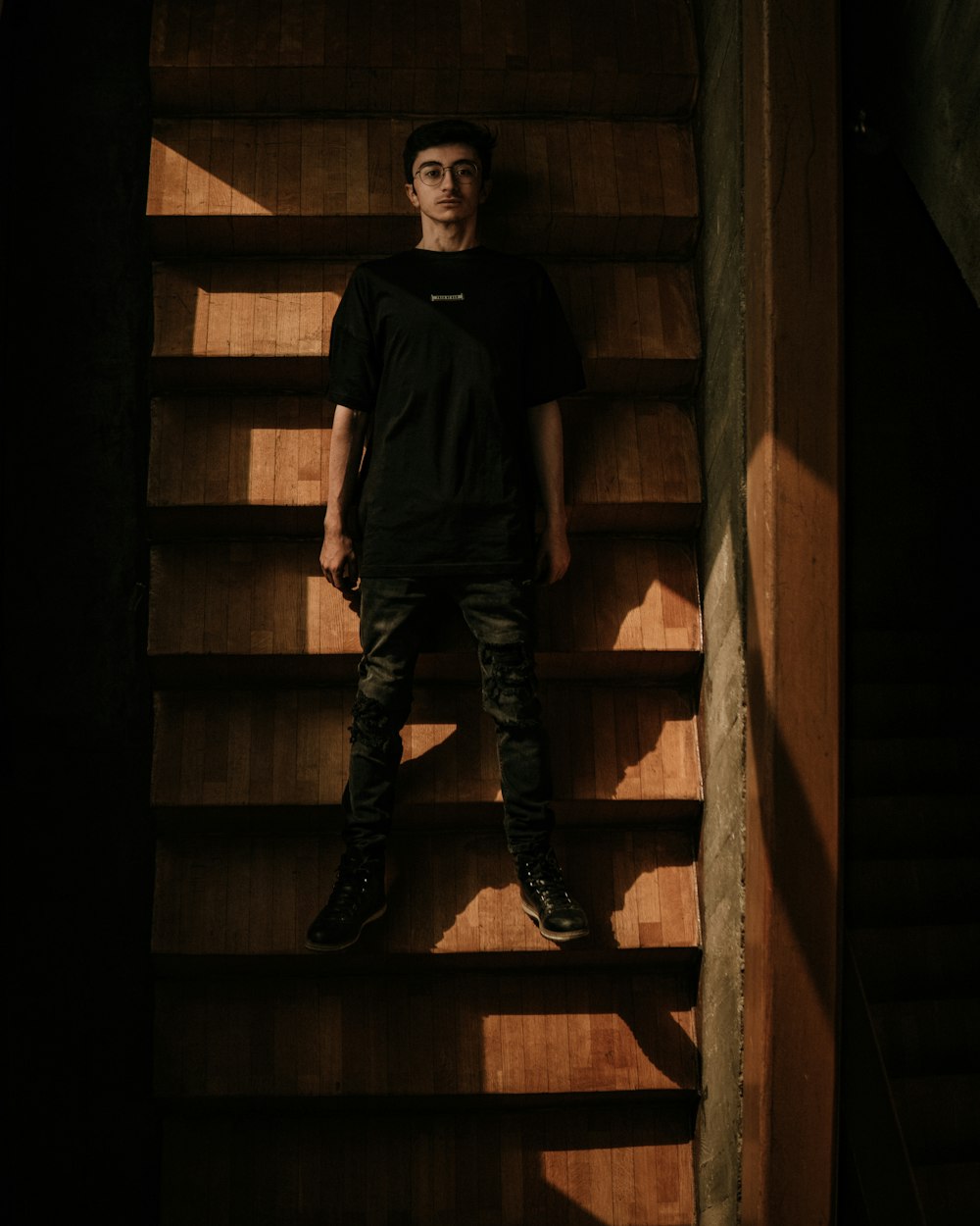 man in black crew neck t-shirt and black and white pants standing on brown wooden