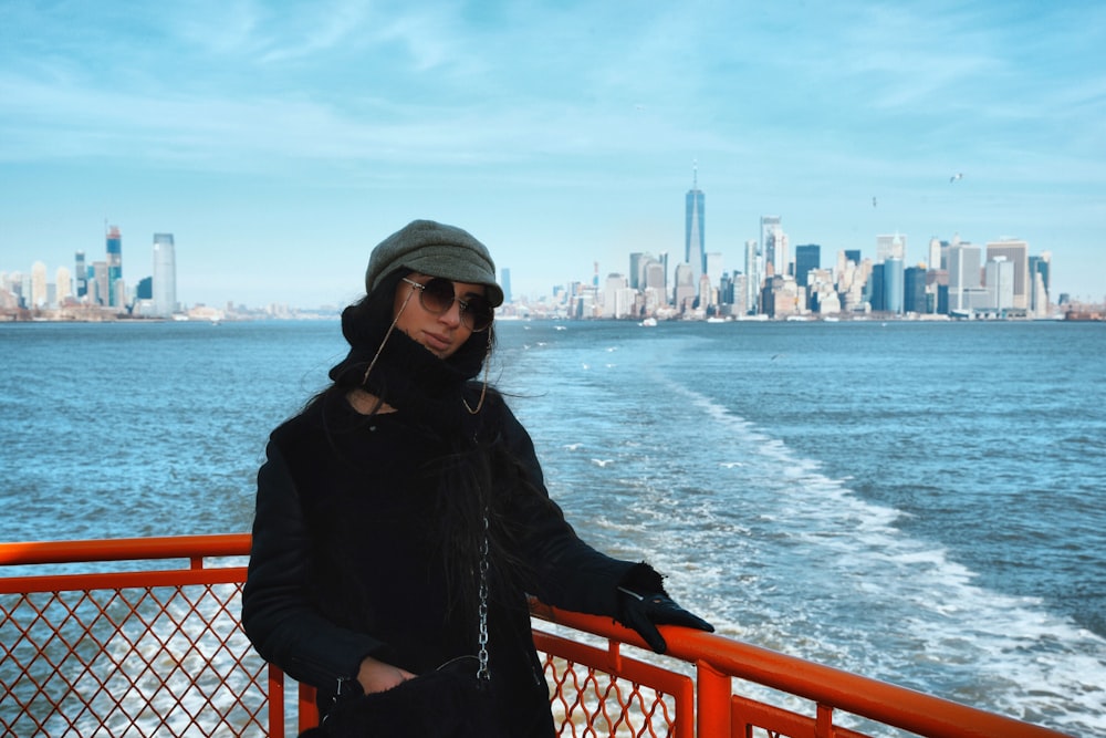 woman in black coat and gray knit cap standing on red metal fence near body of near on with near