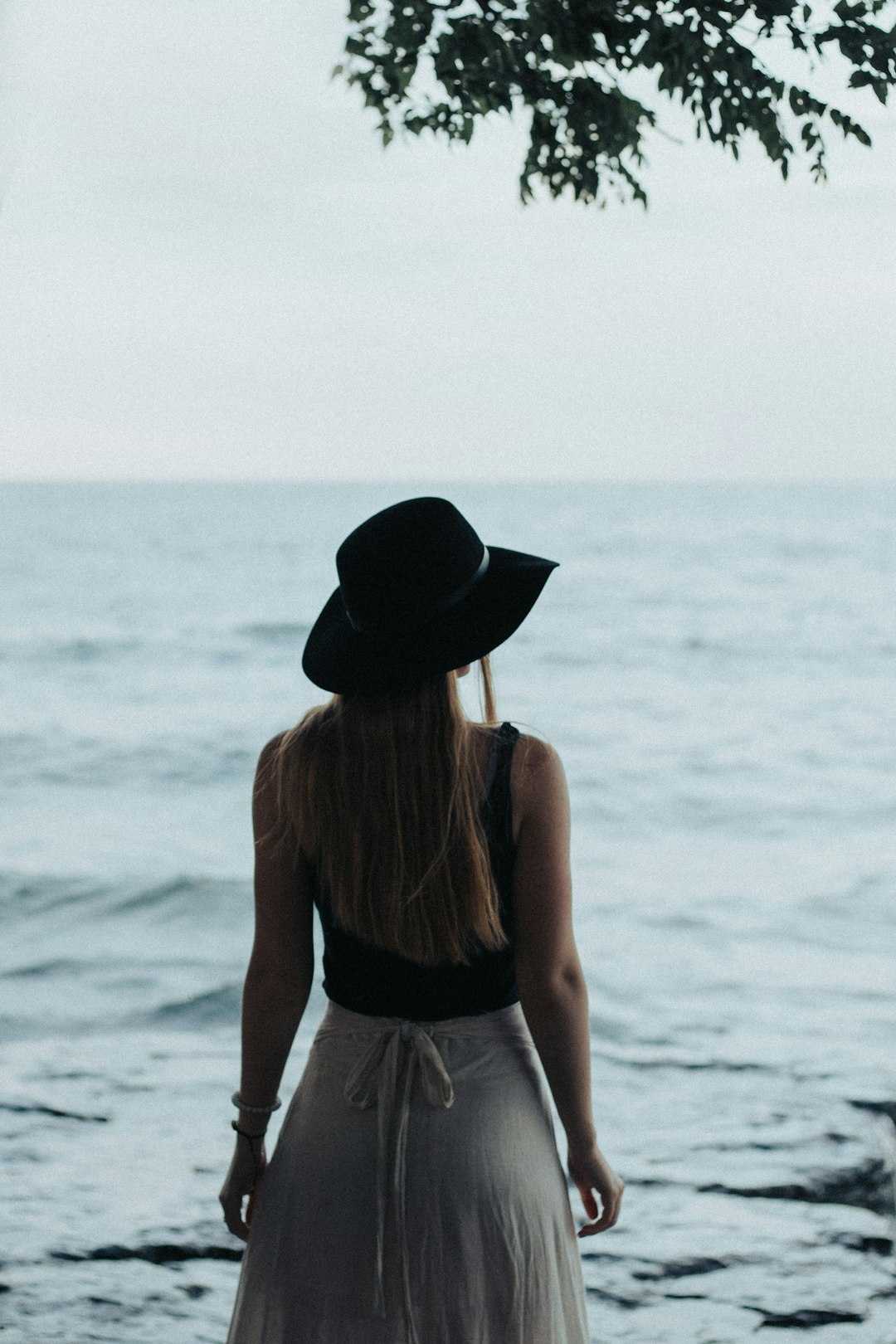 woman in black hat and black tank top standing on beach during daytime