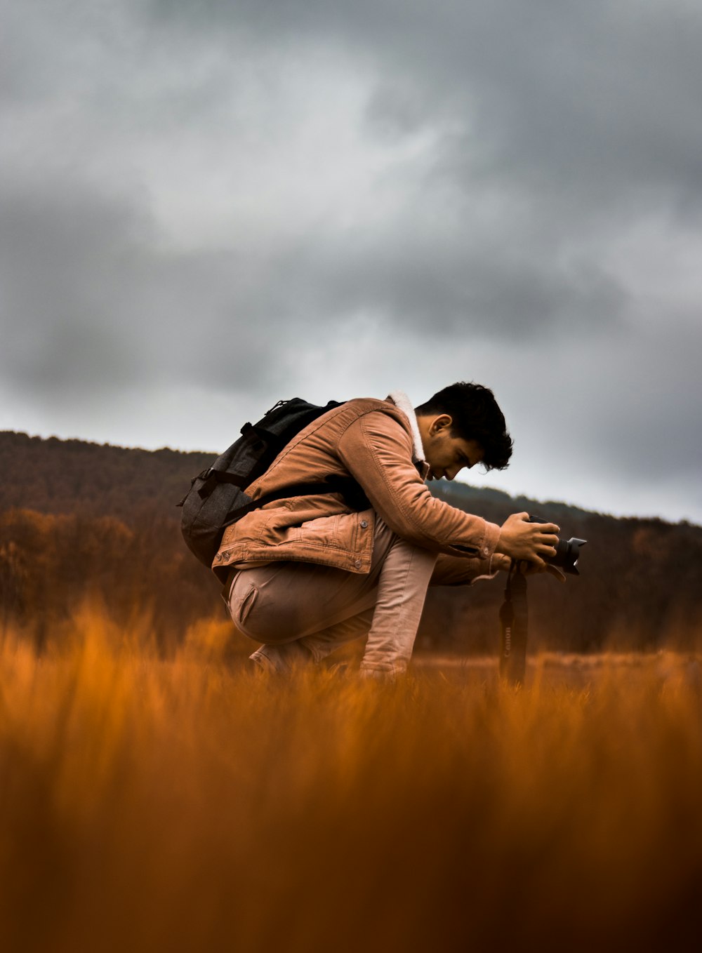 man in brown jacket carrying black backpack on brown grass field during daytime