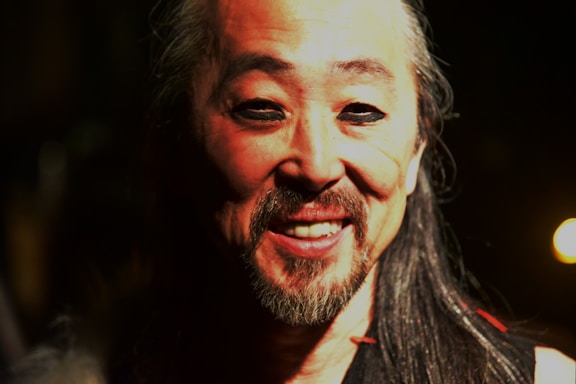 A warm, inviting photo of Sami Ur Rahman behind his camera, smiling gently.