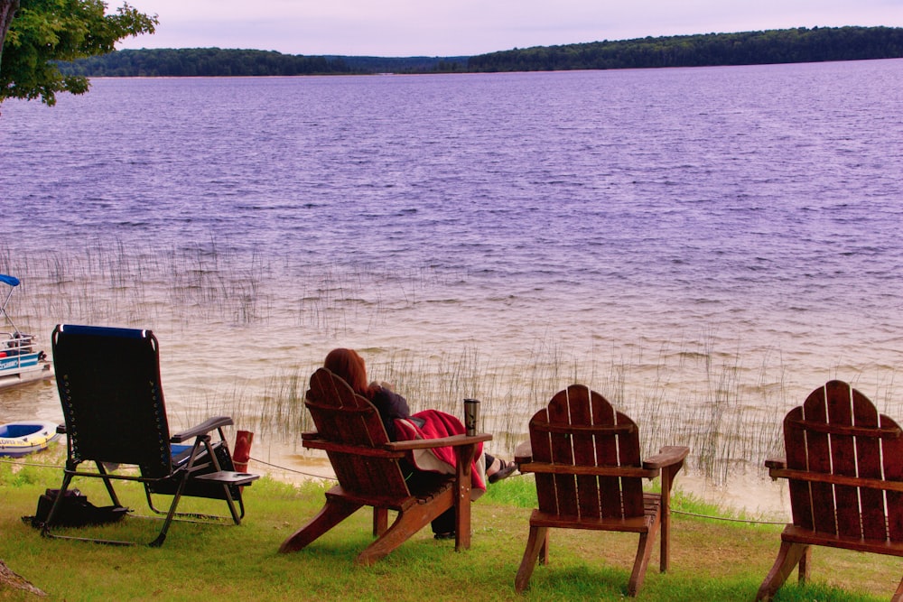 2 person sitting on brown wooden chair near body of water during daytime