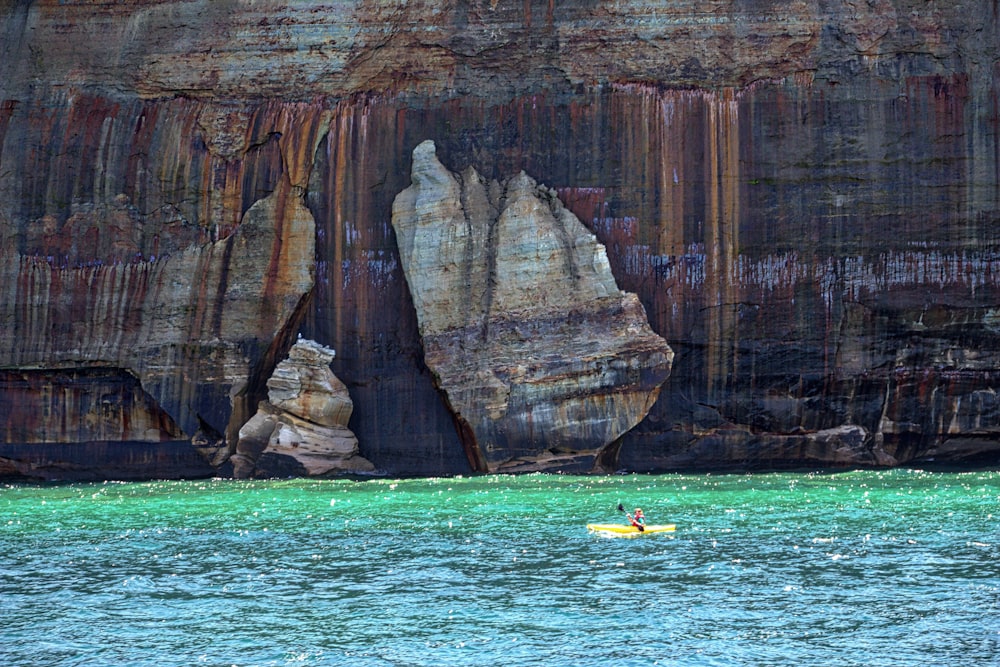 person in yellow kayak on blue sea water near brown rock formation during daytime