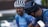 Two cyclists are interacting, both wearing helmets and blue cycling jerseys. One cyclist appears to be smiling or laughing, suggesting a lighthearted moment. The setting seems to be outdoors, possibly after a race or training session.
