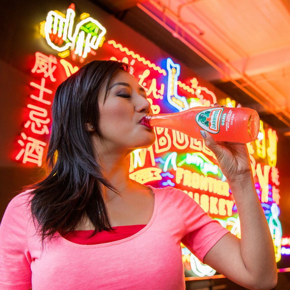 woman in pink crew neck t-shirt drinking from orange plastic bottle