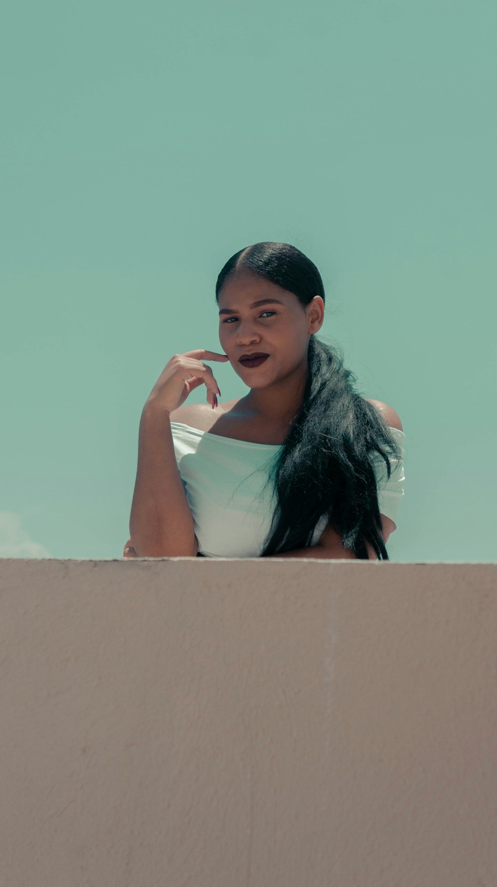 woman in white tank top leaning on brown concrete wall during daytime