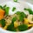 A vibrant bowl of food featuring a creamy topping, fresh mint leaves, banana slices, sunflower seeds, and chunks of mango. The dish appears colorful and refreshing, garnished with an assortment of seeds and oats.