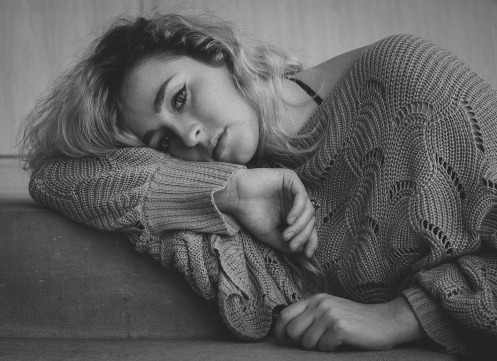 grayscale photo of woman in sweater lying on bed