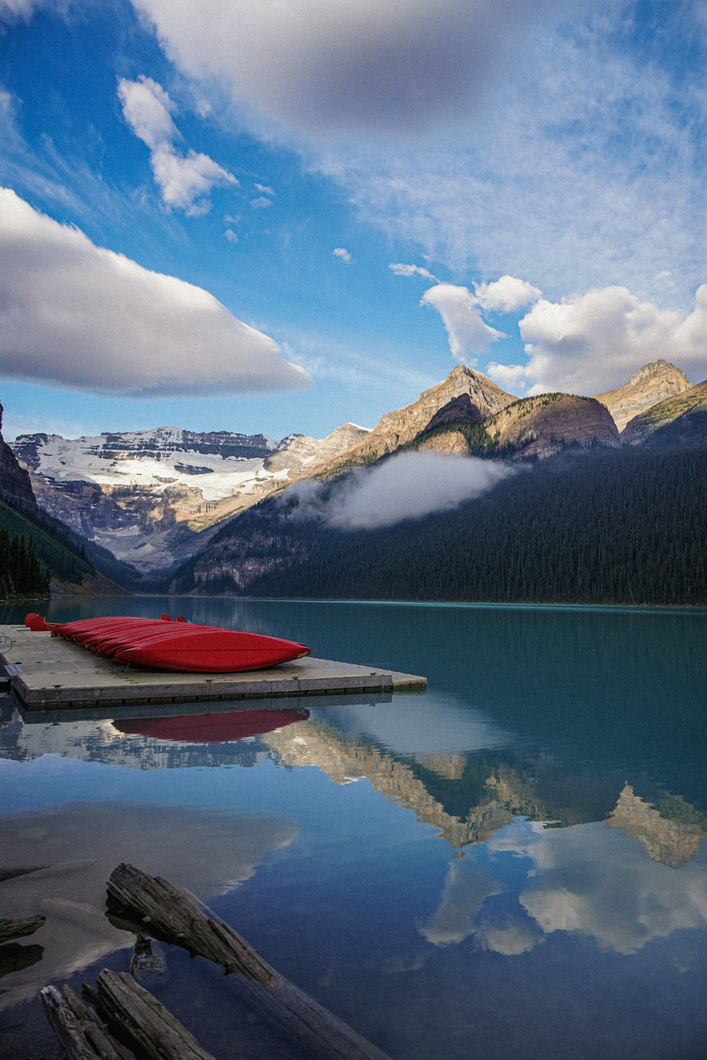 red boat on lake near snow covered mountain under blue sky and white clouds during daytime