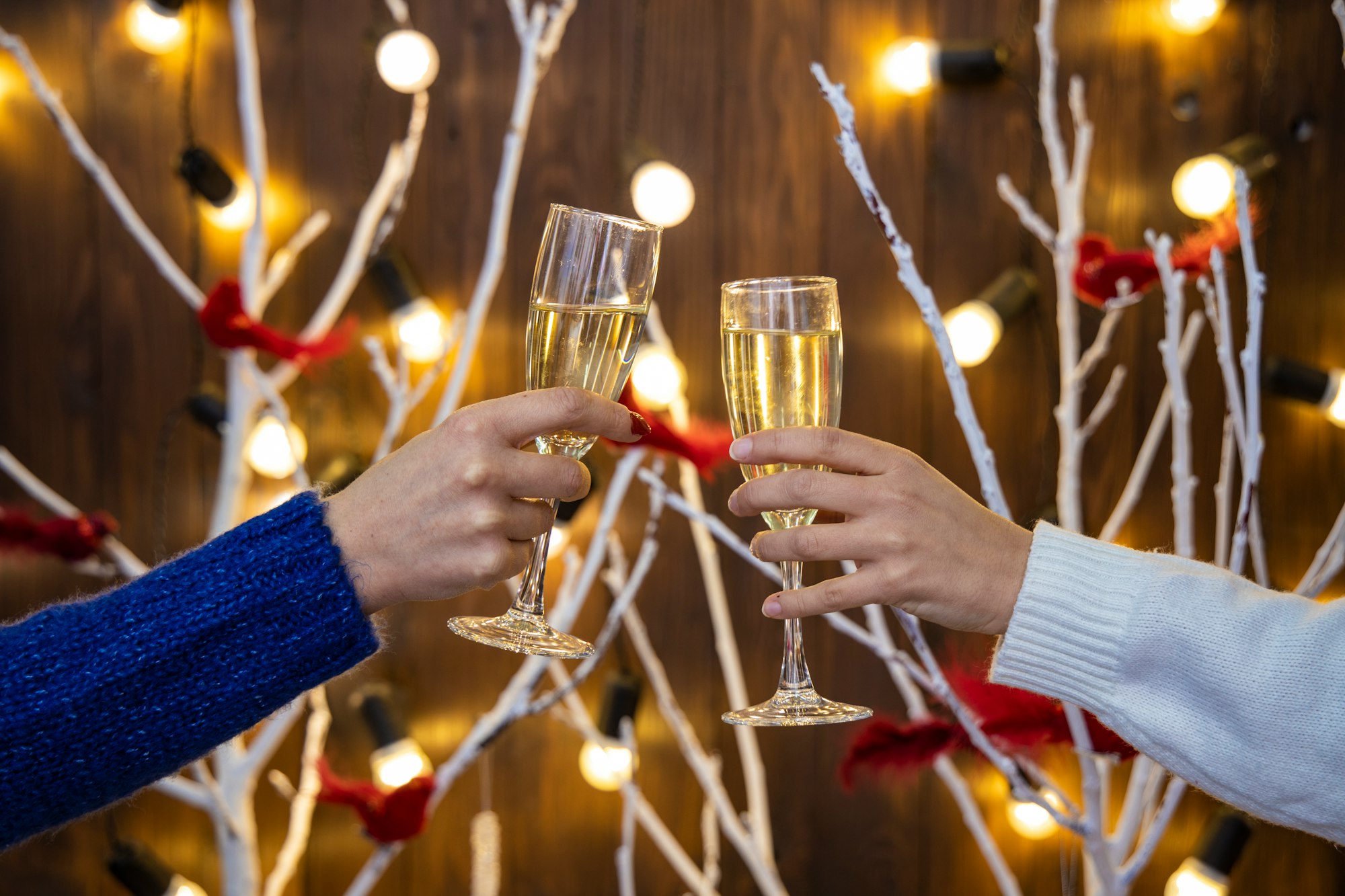 champagne glasses in women hands on Christmas lights festive room decorated background indoor view holidays eve time 