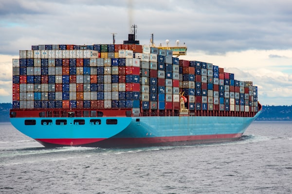 A container ship loaded with stacks of containers traverses grey waters. 