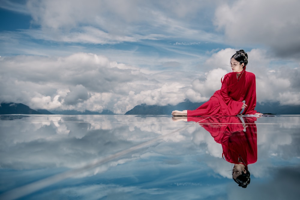 woman in red jacket and black pants standing on rock under white clouds and blue sky