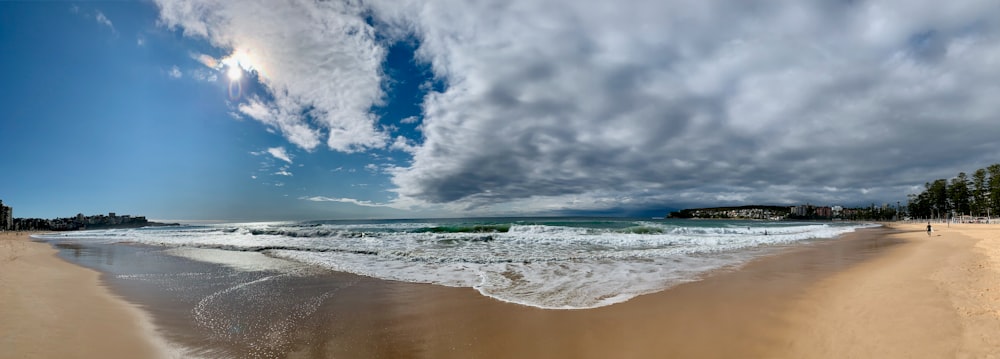olas del océano rompiendo en la costa bajo el cielo nublado azul y blanco durante el día