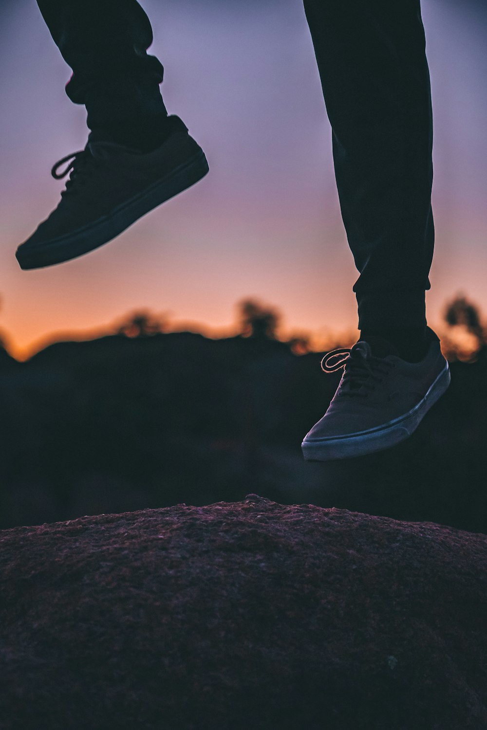 person wearing black pants and black shoes standing on rock during sunset
